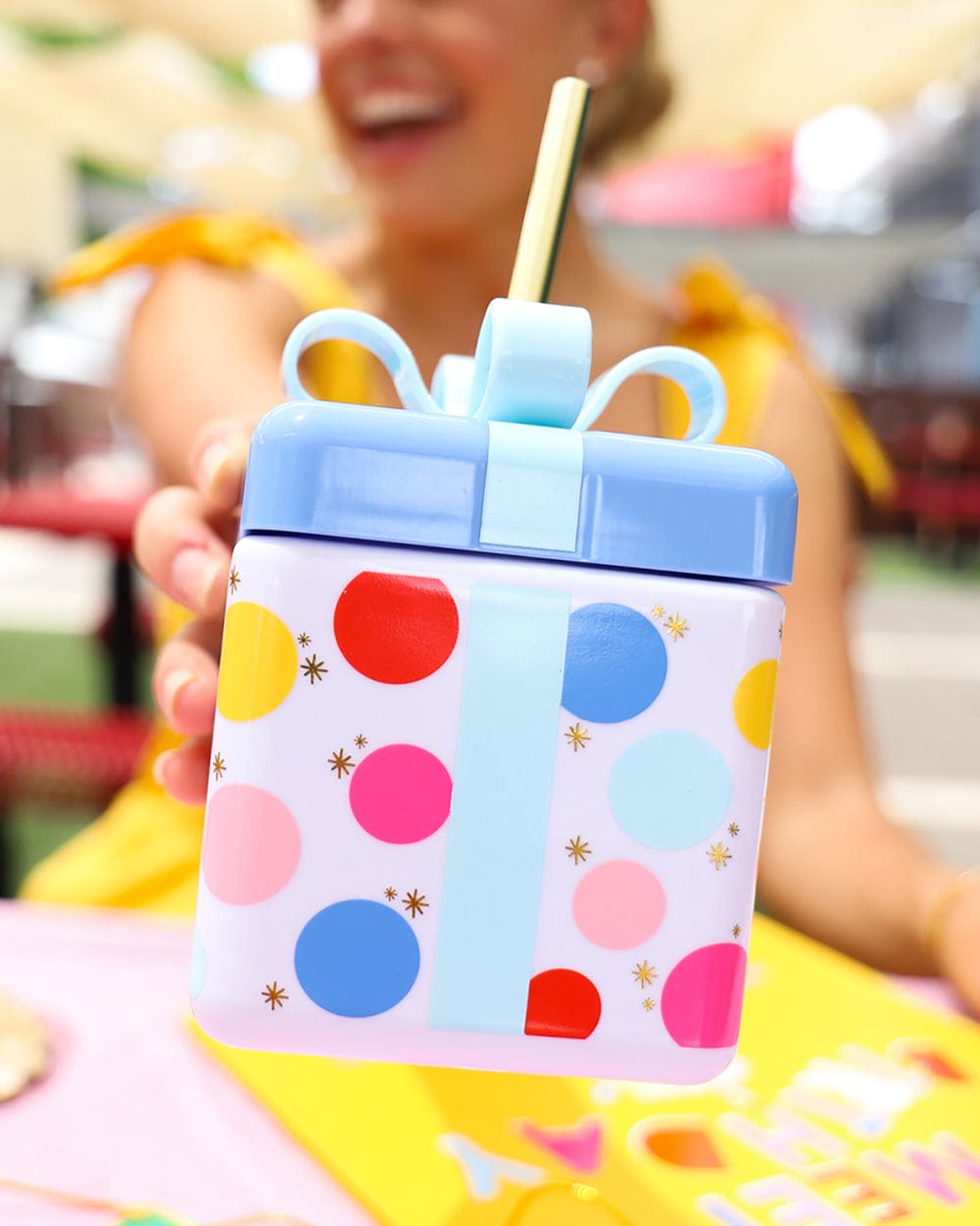 Girl holding birthday gift cup with colorful polka dots in pink, red, blue, yellow and gold sparkles