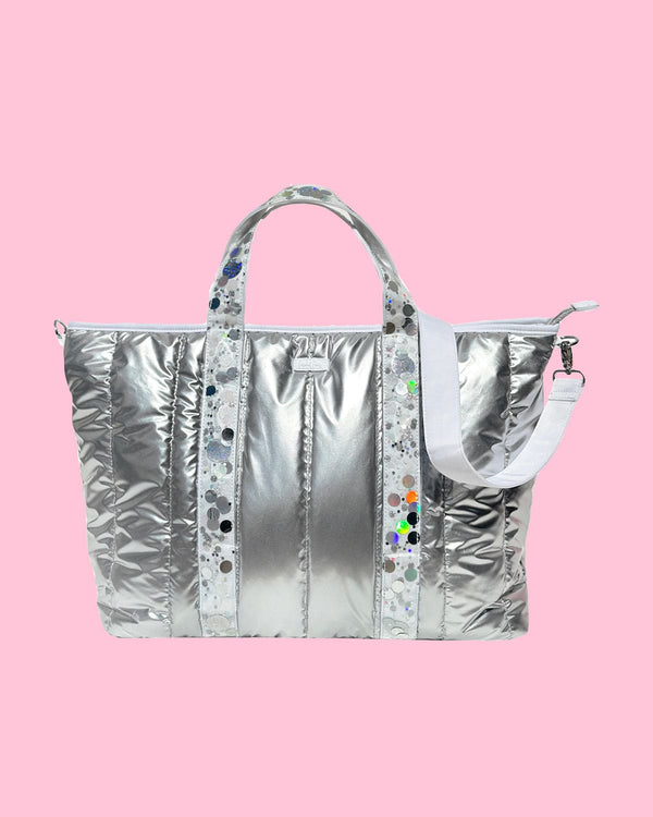 A silver duffle bag with iridescent confetti straps and a white detachable shoulder strap.