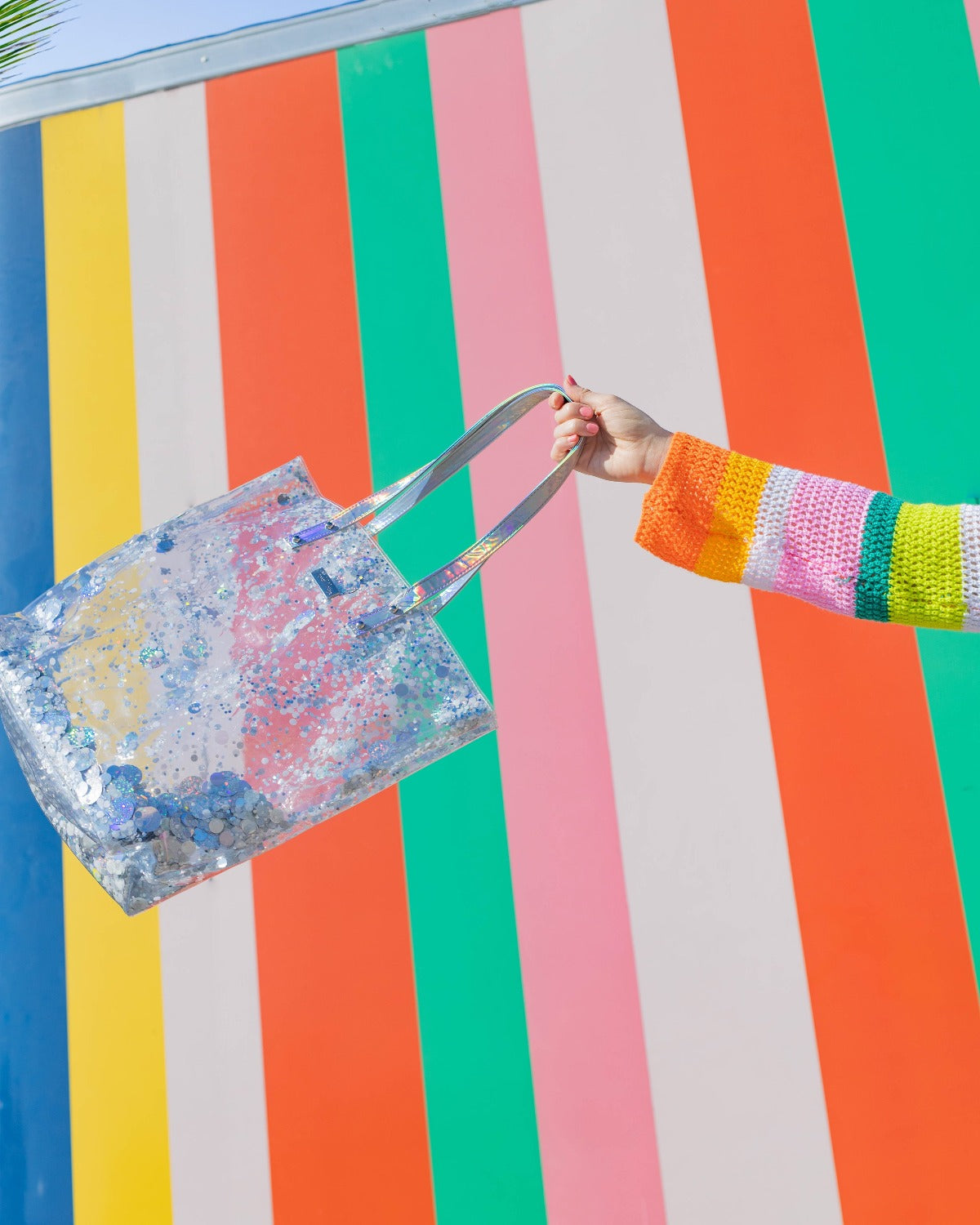 A clear, silver confetti tote bag with iridescent straps.