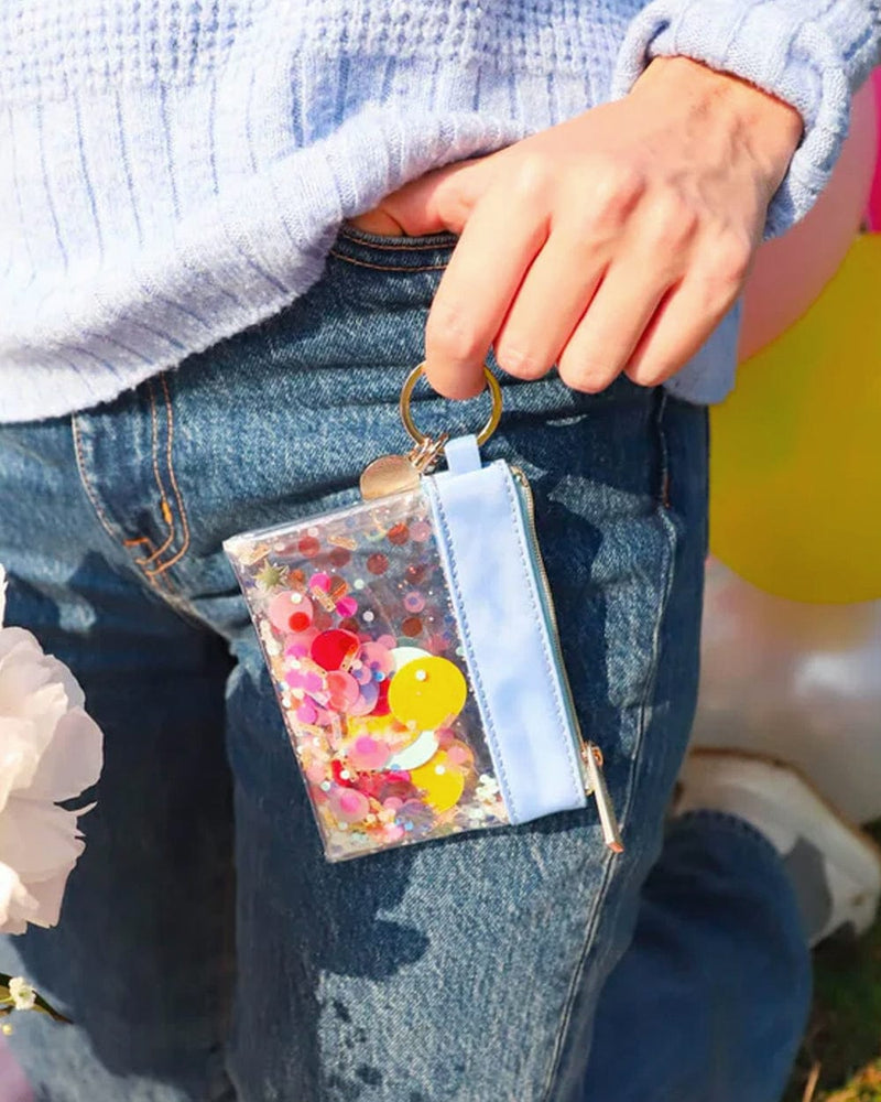 Girl wearing light blue sweater holding mini wallet keychain showing off confetti, nylon lining and gold hardware and finishes