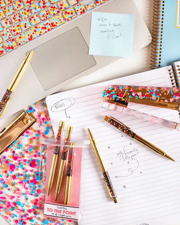 Set of three gold, colorful confetti ballpoint pens at the office. note pad, stapler, laptop and notebook.