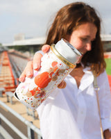 Brunette woman holding a can with an orange can cooler in the bleachers at a stadium