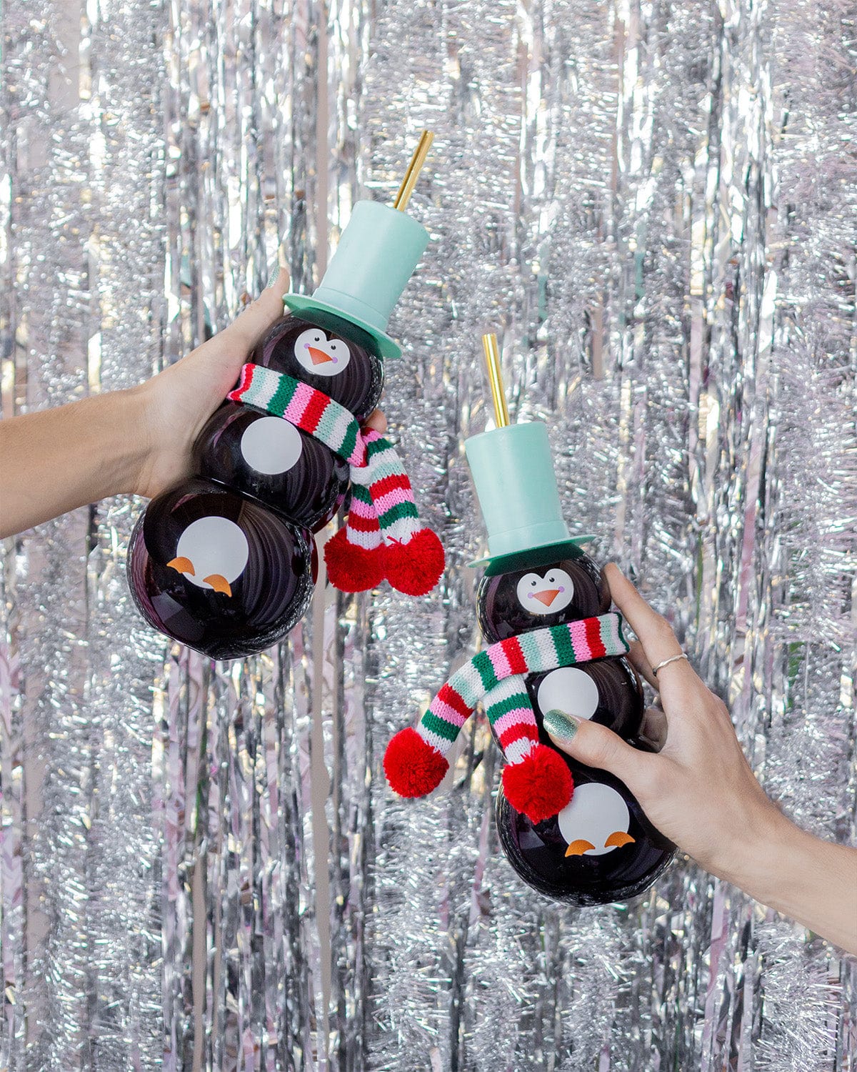 Hands holding Penguin Sippers shot against silver tinsel background.