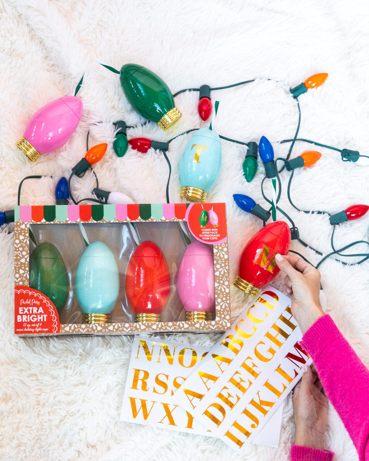 Hand placing sticker of red sipper with sipper set and light bulbs shot against white fur background. 
