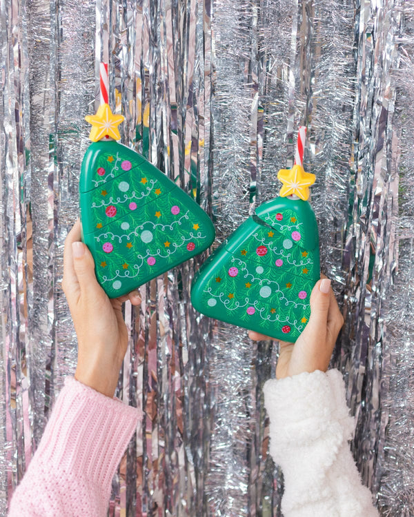 Two Christmas tree shaped novelty sippers in front of a silver tinsel background.
