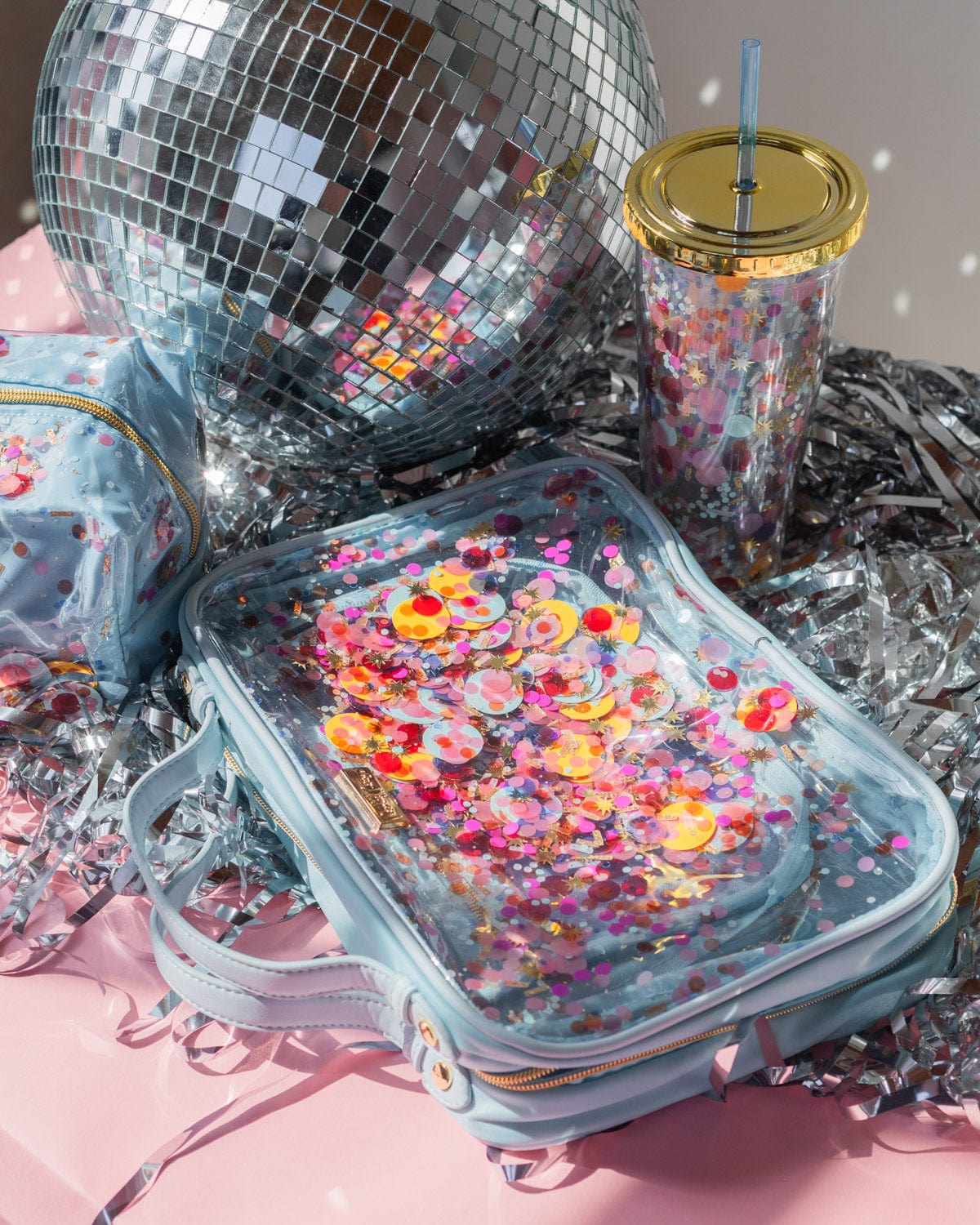 Traveler cosmetic bag case on its side showcasing colorful confetti mix next to a disco ball and pink background.