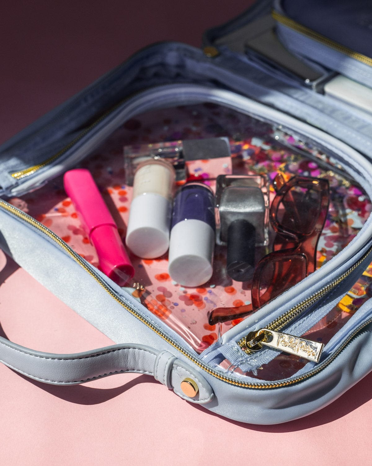 Beauty makeup products and sunglasses in cosmetic bag open in half with gold hardware and luxe zipper.