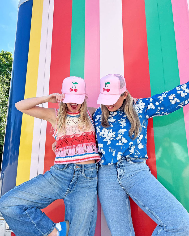 two girls smiling with very cherry trucker hats in front of colorful striped wall