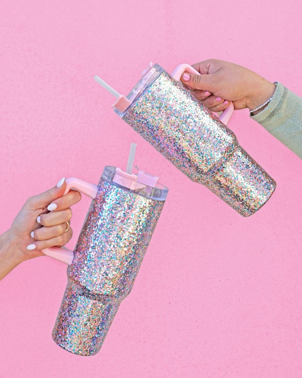 two Stainless steel glitter tumblers with pink handles and lid against pink wall