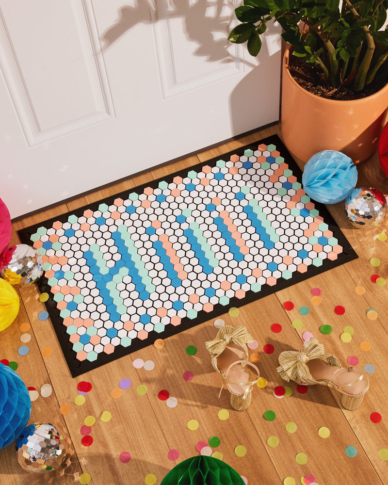 Door mat with hexagon tiles spelling out Hiii on wooden floor with confetti and disco