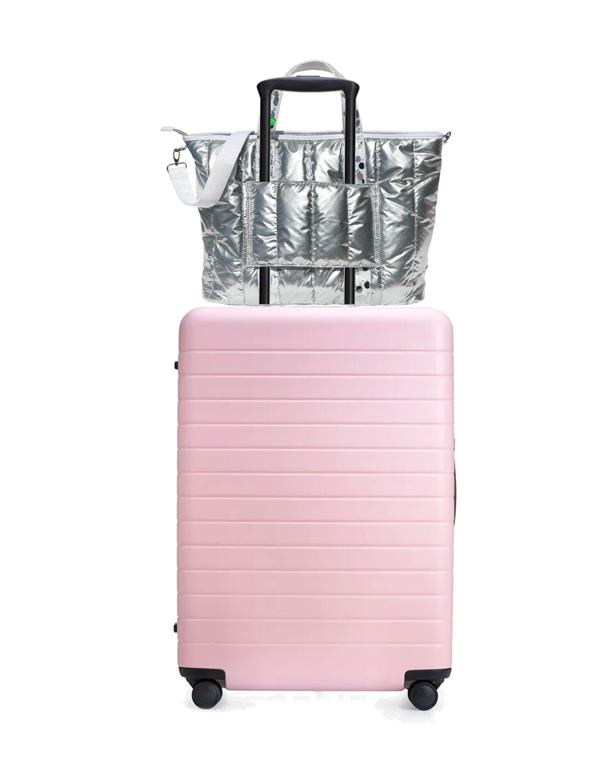 A silver duffle bag with iridescent confetti straps and a white detachable shoulder strap.