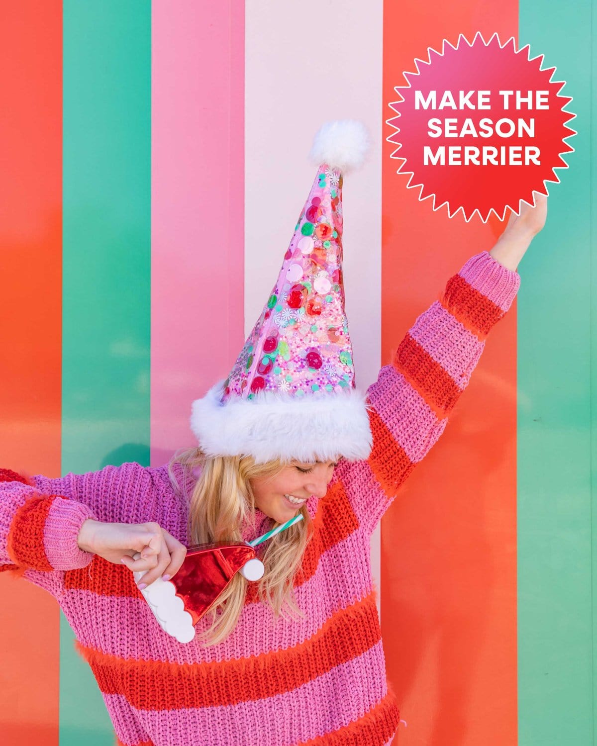 Woman smiling with Santa Sipper in her and and pink confetti Santa Hat shot against colorful striped wall. Text reads "Make the season merrier." 