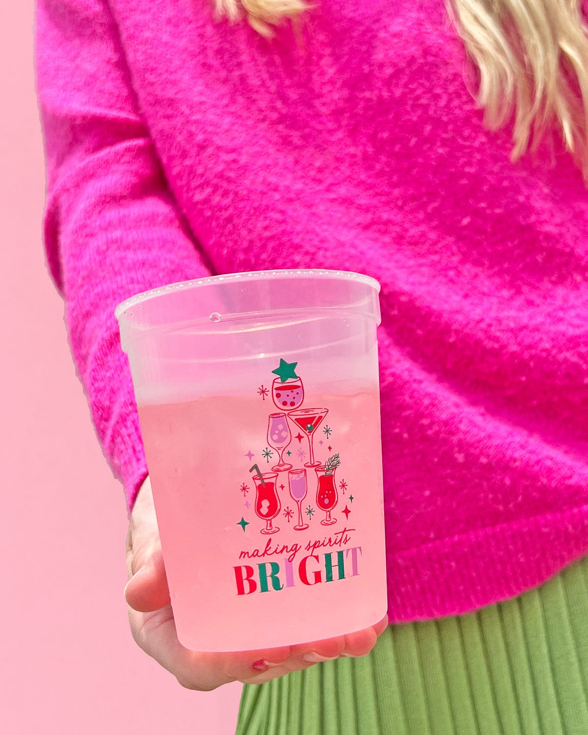 Woman holding 'Making Spirits Bright' color-changing cup with a pink background. 