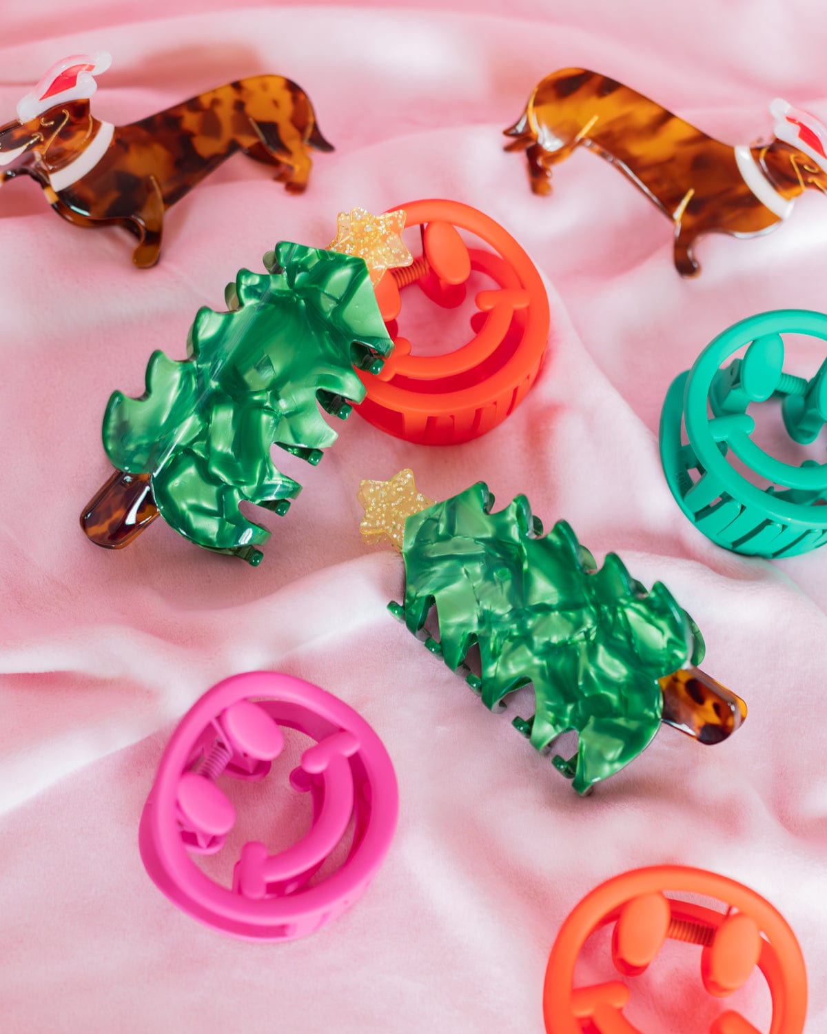 Christmas tree claw clips among assortment of holiday claw clips shot against pink background. 