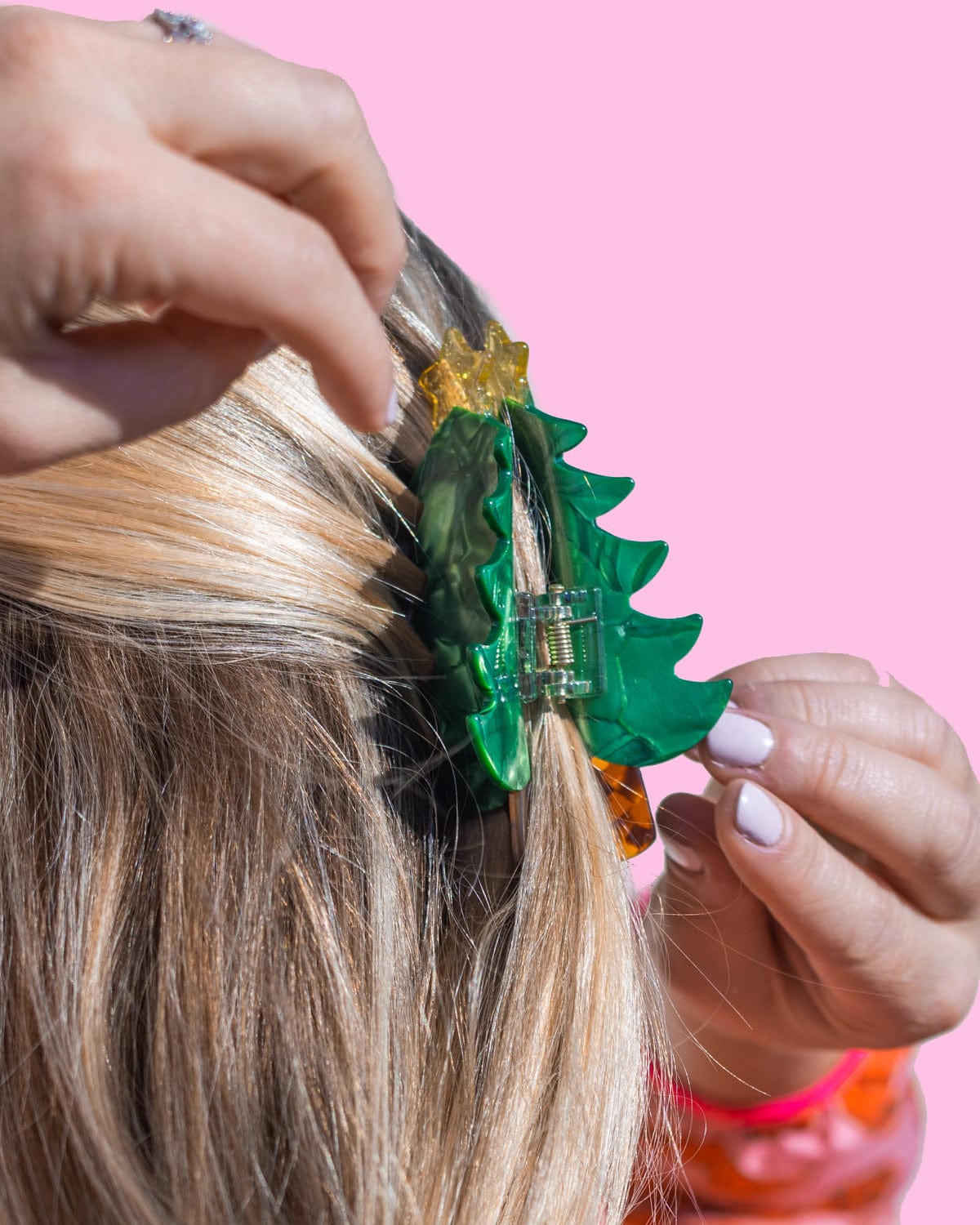 Christmas tree claw clip being placed into hair shot against pink background. 