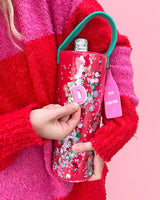 Women placing sticker onto trapped confetti wine bag shot against pink background. 