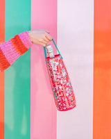 Bottle of champagne in trapped confetti wine tote being held in air shot against colorful striped background. 