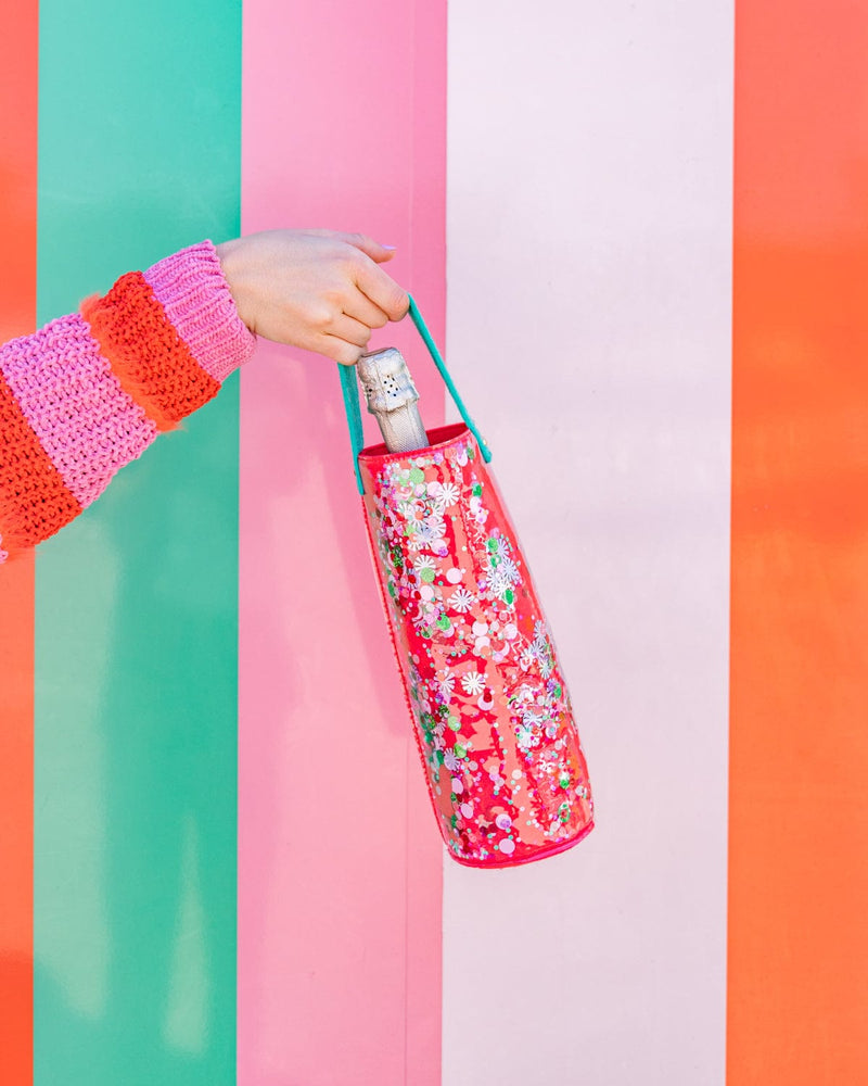 Bottle of champagne in trapped confetti wine tote being held in air shot against colorful striped background. 