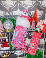 Woman placing bottle into confetti wine bag with display of confetti stocking, holiday sippers, and holiday decor. 