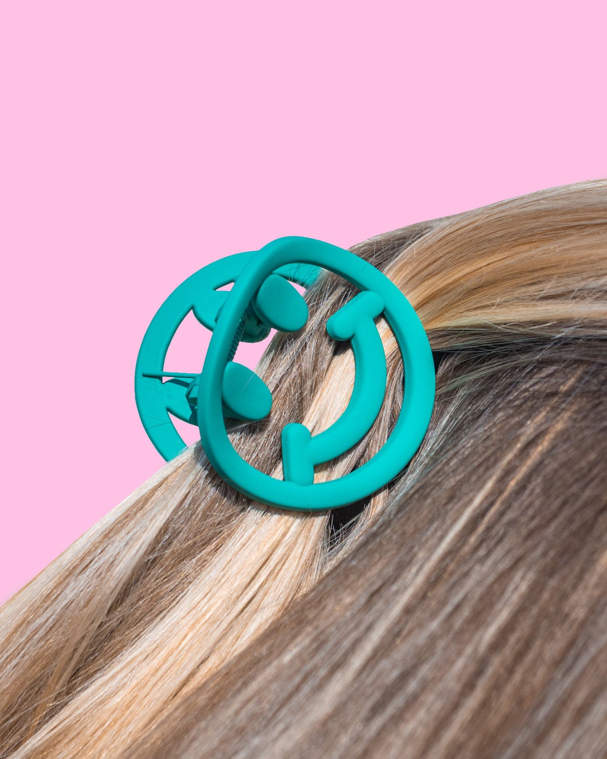 Green smiley claw clip placed into hair shot against pink background. 