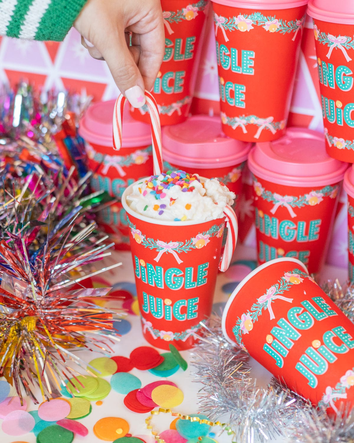 Hand placing candy into 'Jingle Juice' red to-go cup in assortment of cups and confetti. 