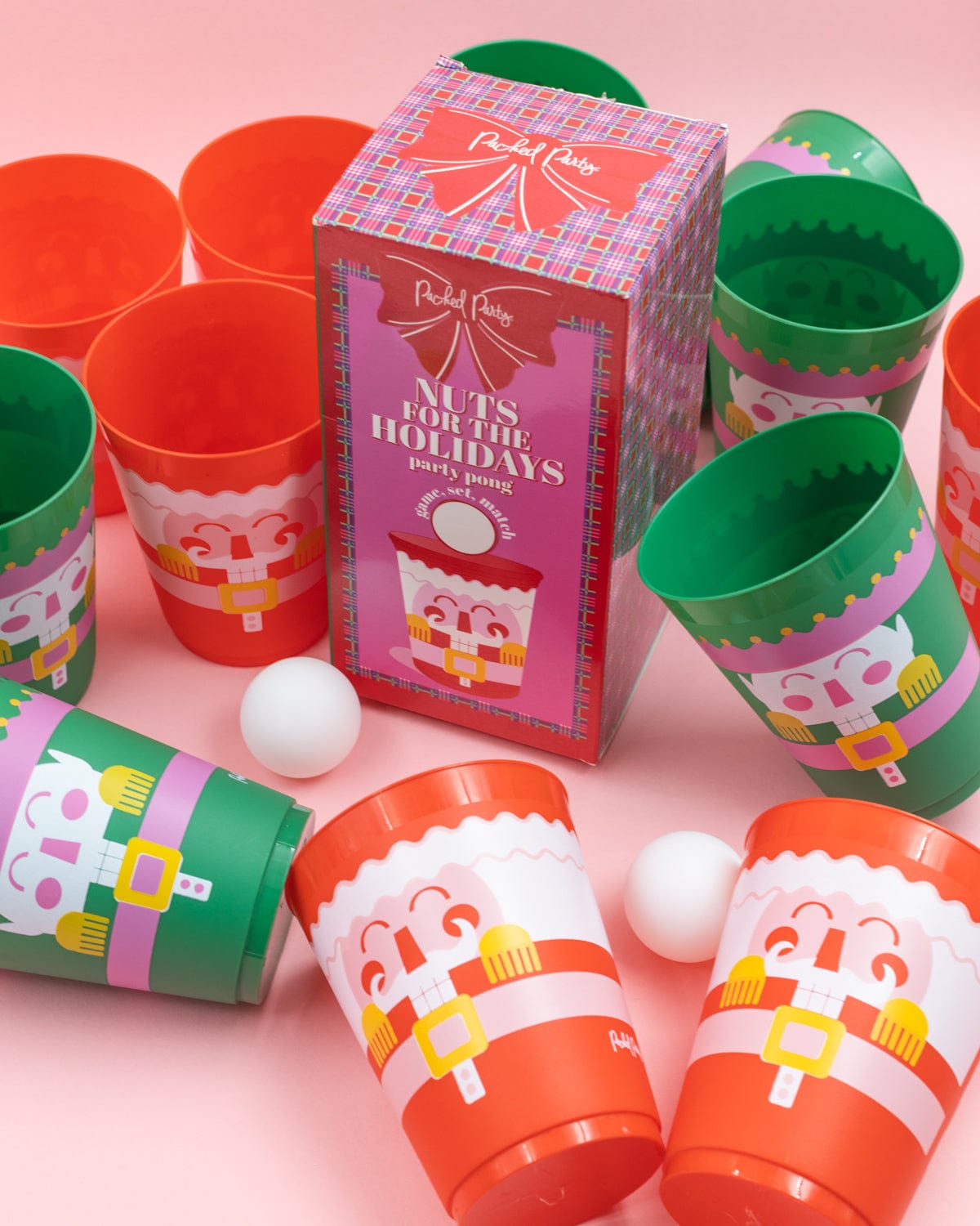 'Nuts for the Holidays' pong set with assortment of cups and ping pong balls shot against pink background. 