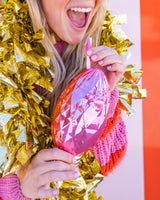 Woman holding pink faceted light bulb sipper shot against striped wall. 