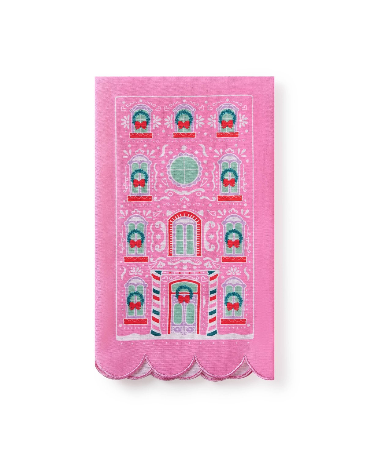 Pink tea towel with printed gingerbread house and scalloped edge detail shot against white background. 