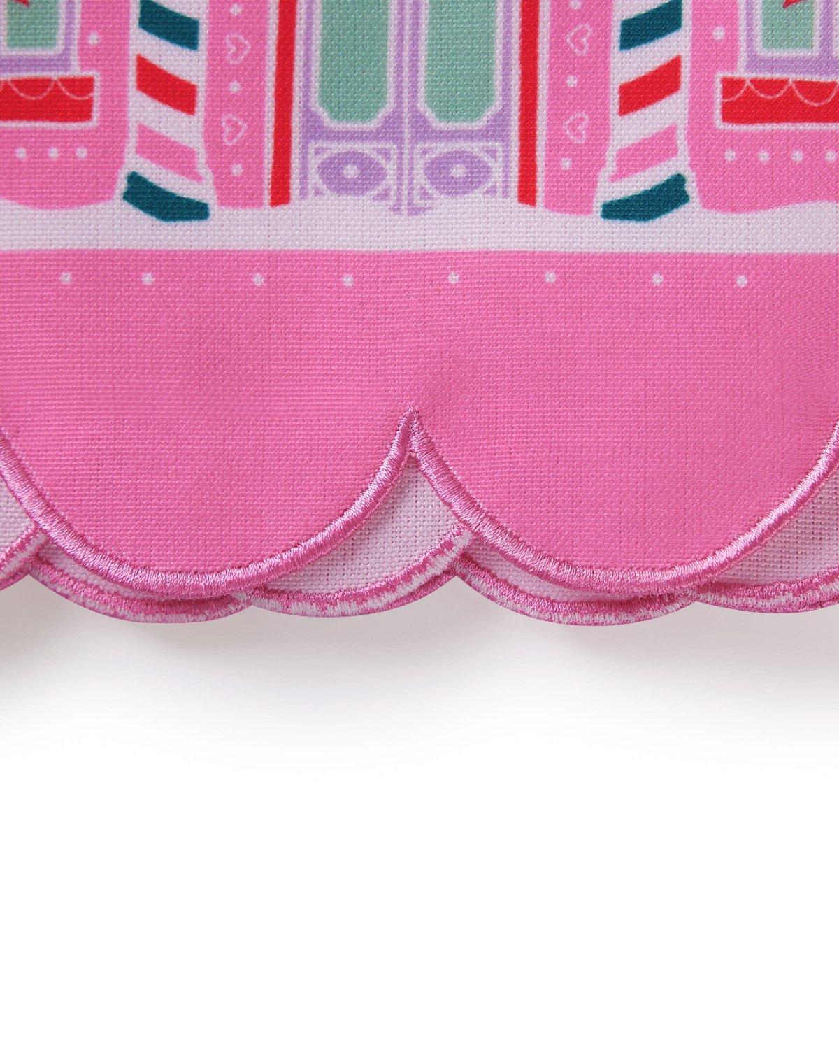 Close up of scalloped edge detail of pink tea towel shot against white background. 