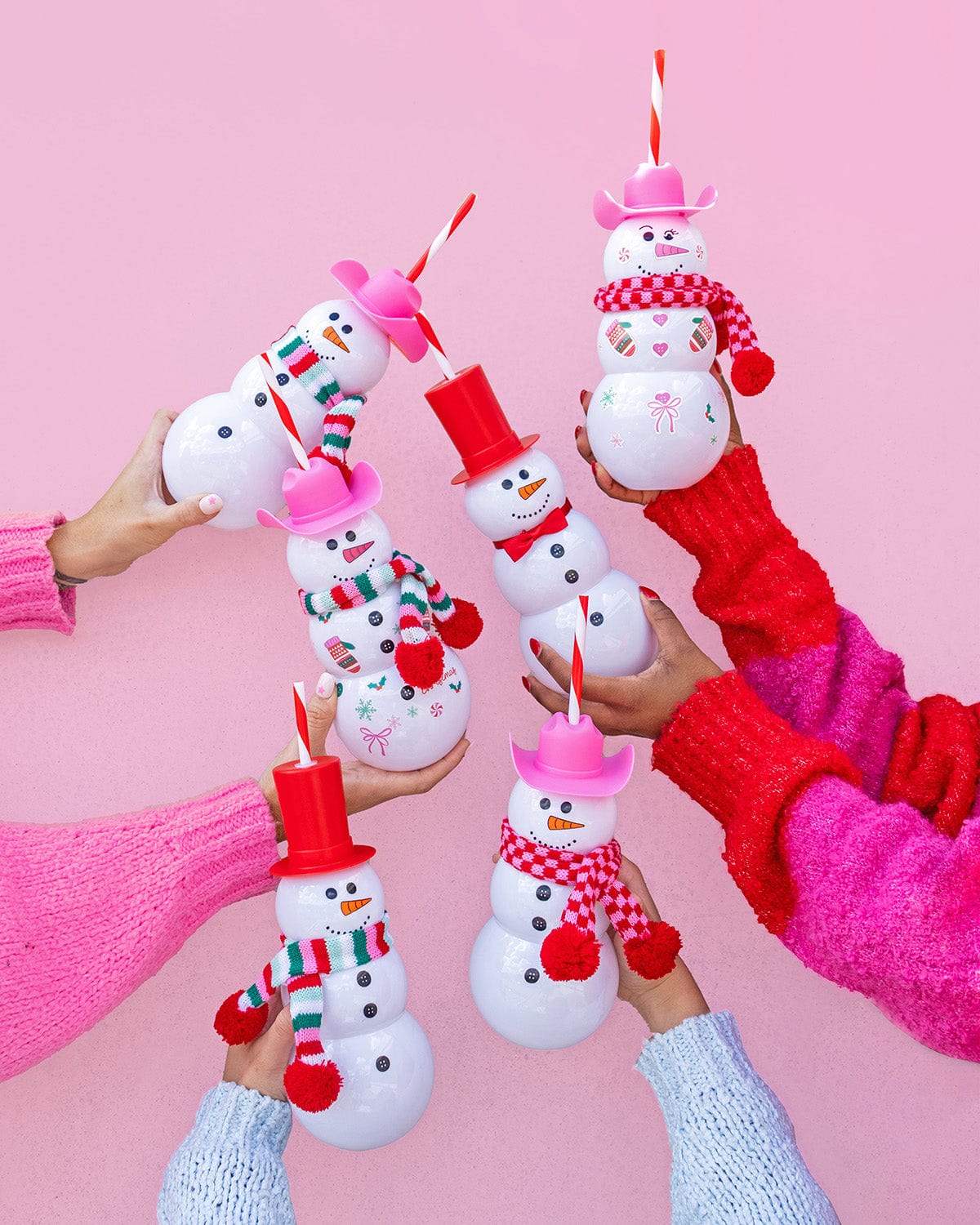 Hands holding Snowman Sippers in air shot against pink background. 