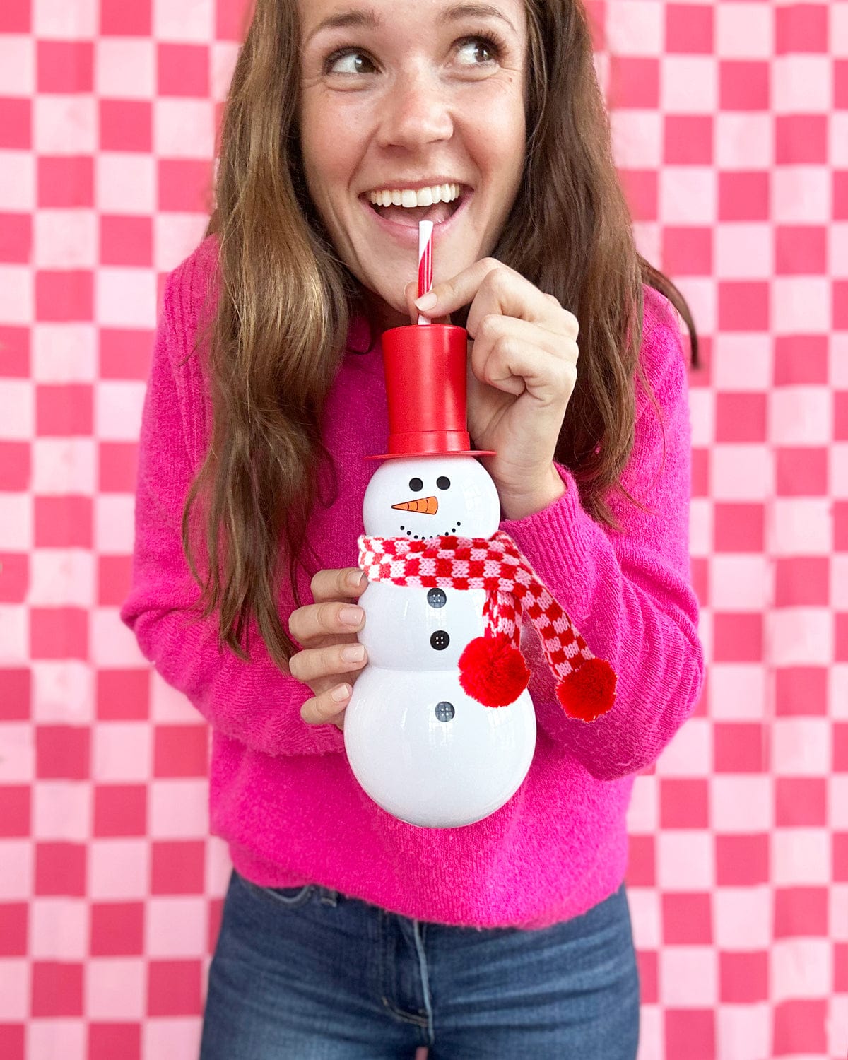 Woman holding Snowman Sipper with checkered scarf shot against pink checkered background. 
