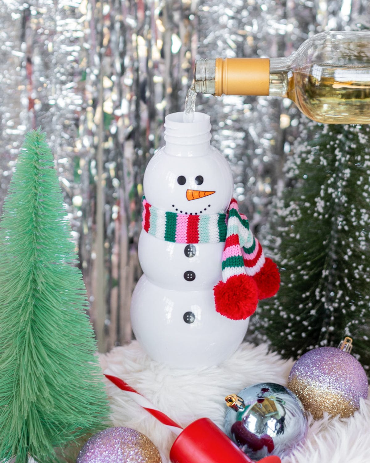 Drink being poured into Snowman Sipper with holiday decor shot against silver tinsel background. 