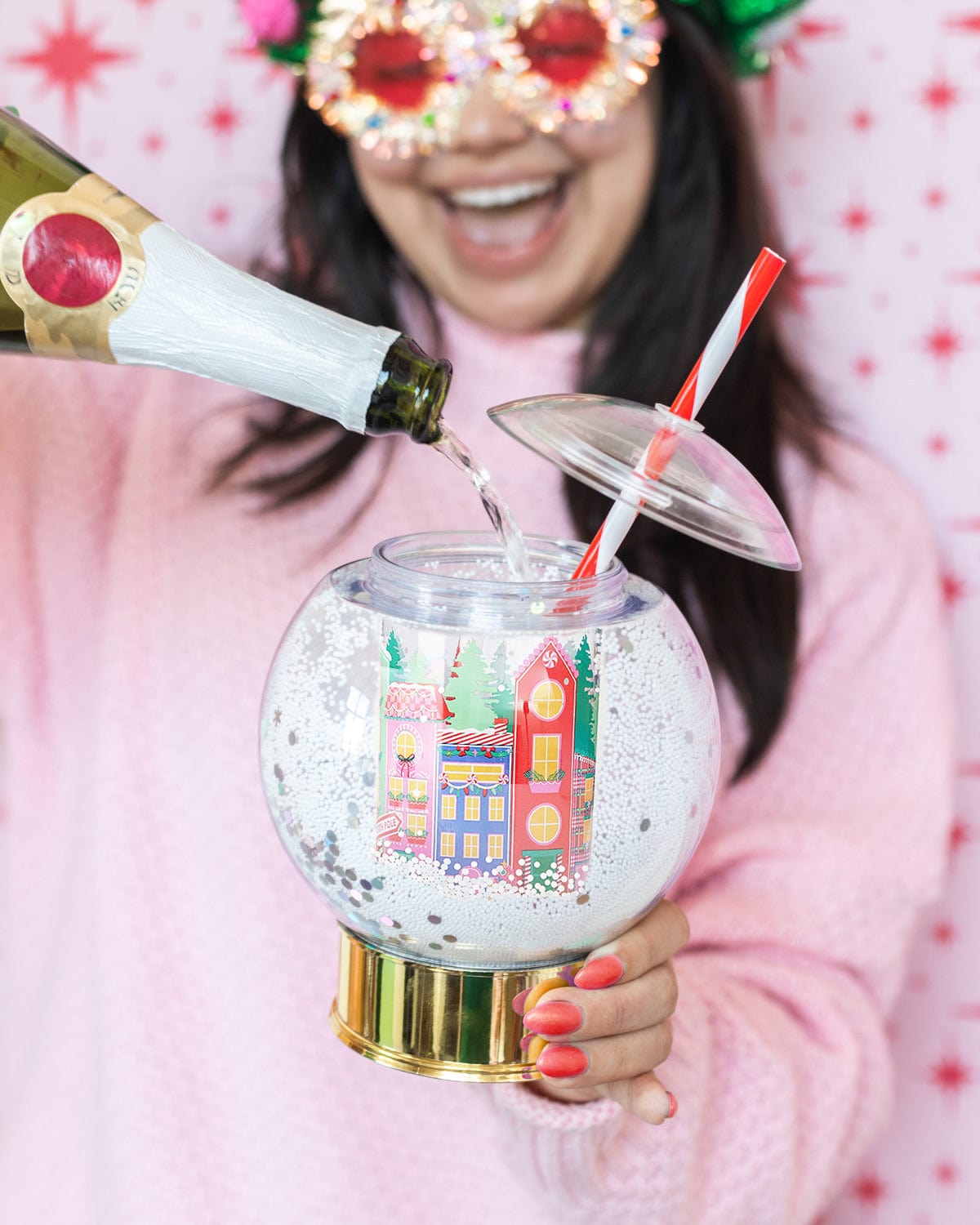 Woman pouring drink into village snow globe sipper white smiling. 