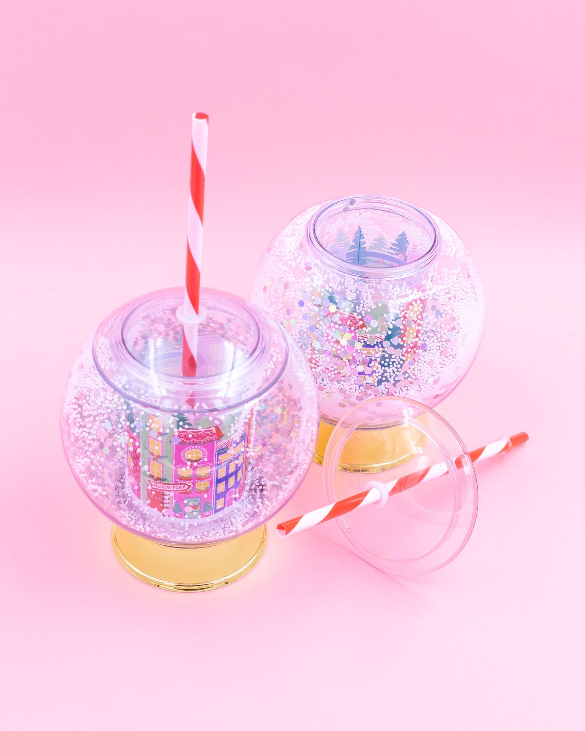 Two village snow globe sippers shot against pink background. 
