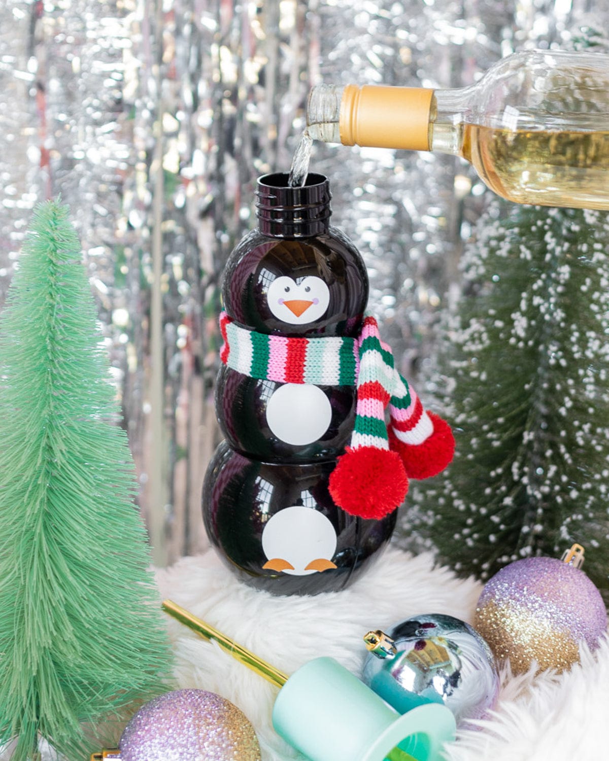 Wine being poured into Penguin Sipper with holiday decor shot against silver tinsel background. 