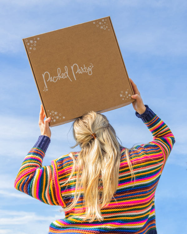 Woman in rainbow sweater holding brown box with Packed Party logo above her head