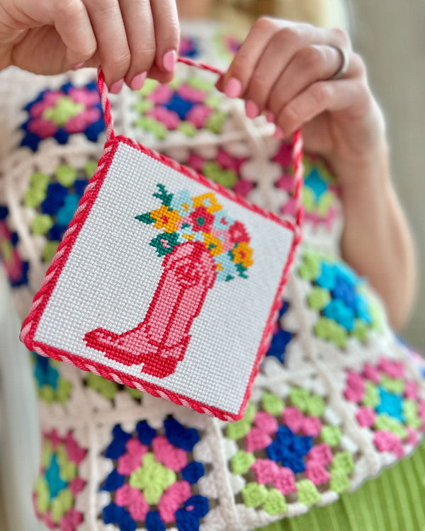 girl holding needlepoint craft in front of her colorful knitted sweater