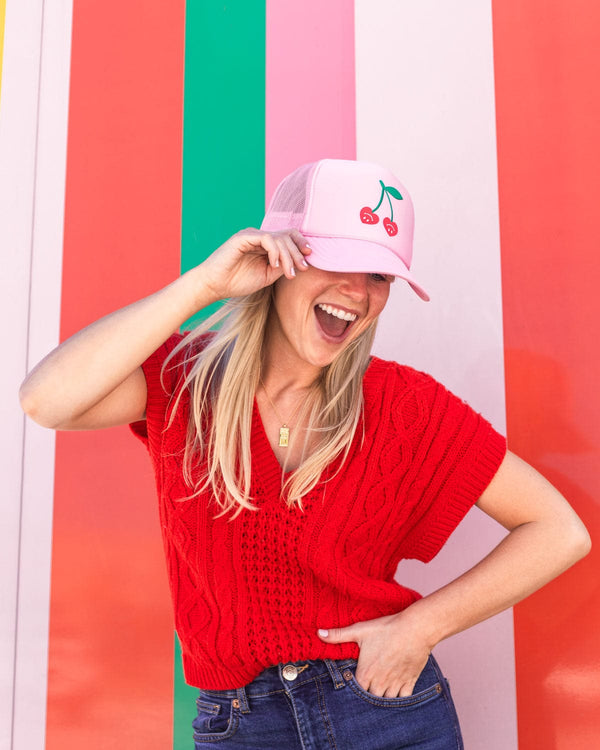 blonde girl smiling and laughing with very cherry trucker hat in front of colorful striped wall