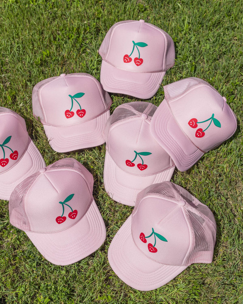 Several very cherry pink trucker hats together in the grass