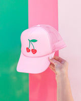 adorable pink trucker hat with unique upside down smile cherries on green stem in front of striped wall