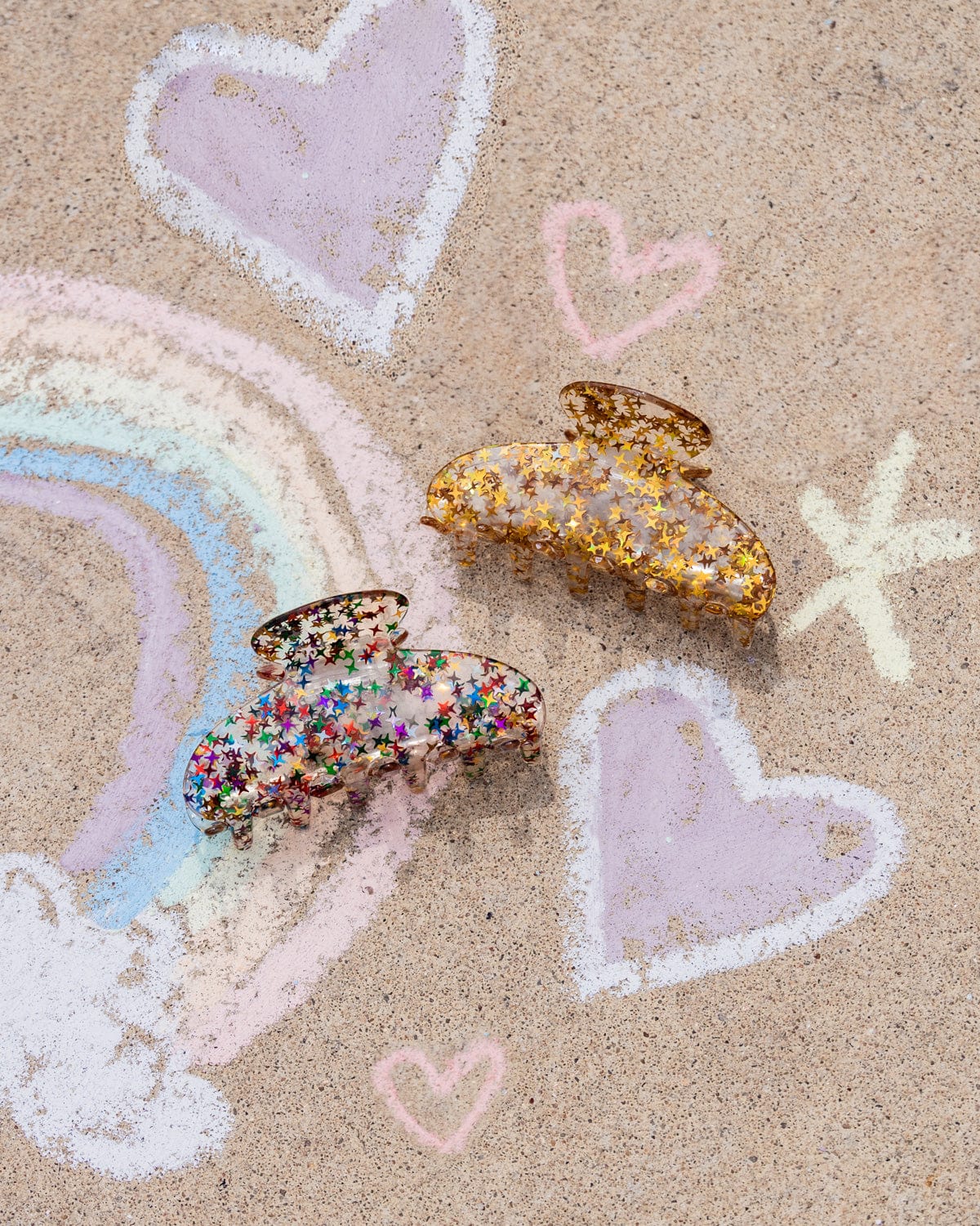 Two star-filled claw clips lie side-by-side on a chalk drawing. 