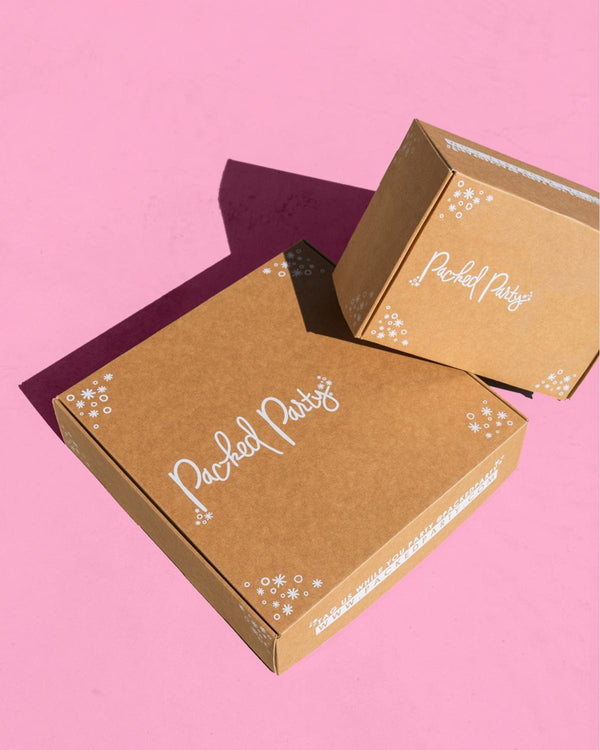 Two brown boxes with Packed Party logo on light pink background