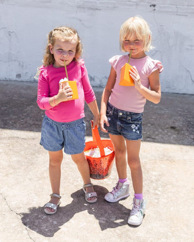 Girls sipping on tumblers holding Halloween trick or treat basket and candy bucket.