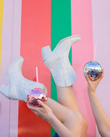 silver and rose gold disco ball shaped cups against striped colorful wall with a girl having fun in her white boots