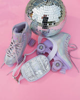 A shiny silver belt bag against pink backdrop with disco ball and roller skates. Shiny and iridescent, metallic colors.