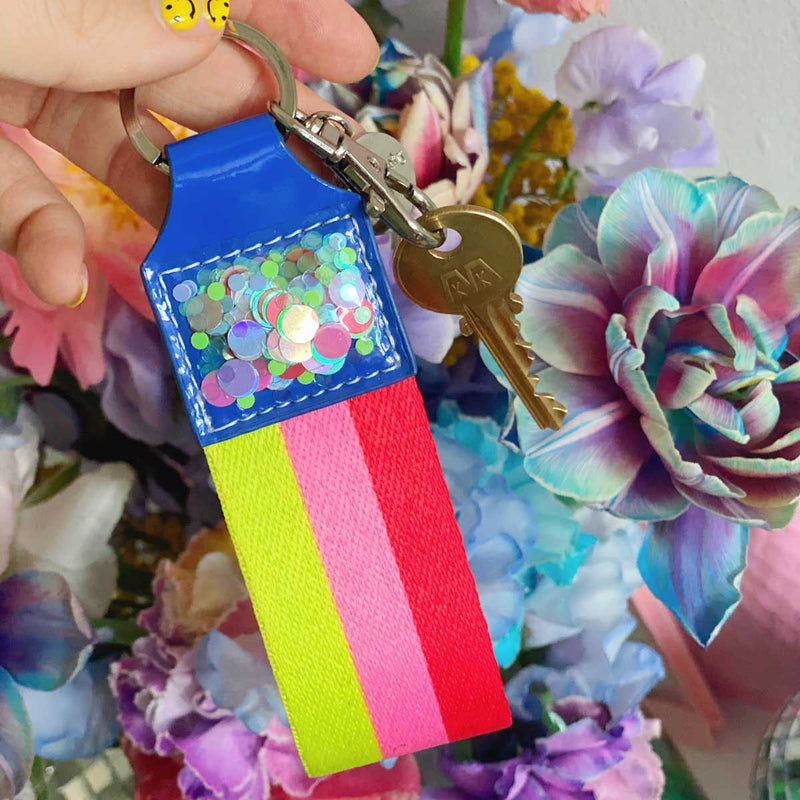 Red, pink, yellow, and blue keychain with confetti in front of flowers.