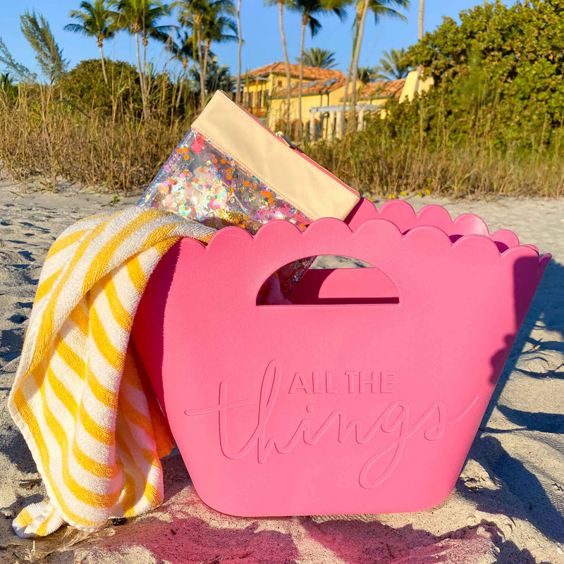 Cute pink jelly tote on a beach with a towel and colorful pouch